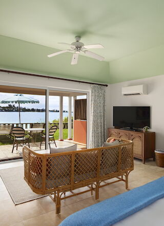 This image shows a cozy, tropical-themed room with a TV, wicker furniture, and a view of the water through sliding glass doors, ending the sentence.