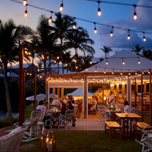 The image shows an outdoor dining area with string lights, people sitting at tables, and palm trees in the background during twilight.