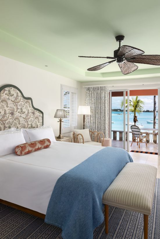 A spacious bedroom with a king-sized bed, elegant decor, ceiling fan, and a view of the ocean through sliding glass doors leading to a balcony.