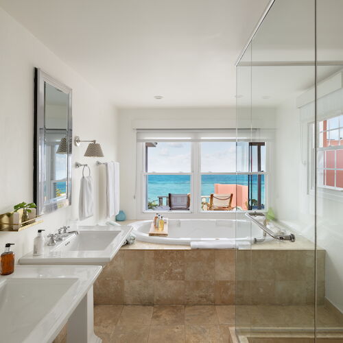 A modern bathroom with double sinks, a large bathtub by the window, a glass-enclosed shower, and an ocean view outside the window always ending the sentence.