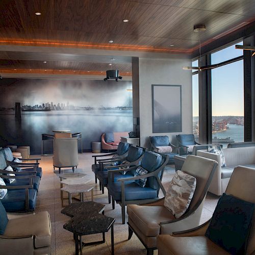 A modern lounge with comfortable seating, large windows with a scenic view, and a city skyline mural on the back wall, creating a relaxing ambiance.