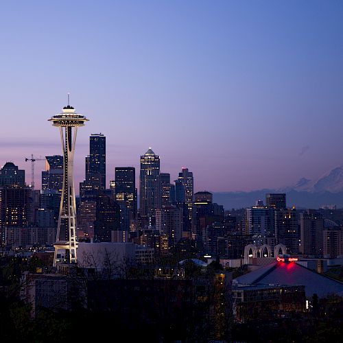 This image shows the Seattle skyline at dusk, featuring the Space Needle prominently with Mt. Rainier visible in the background against a fading sky.