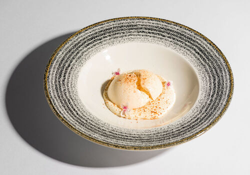 A plated dessert featuring a scoop of ice cream with pink and orange garnish, in a textured bowl.