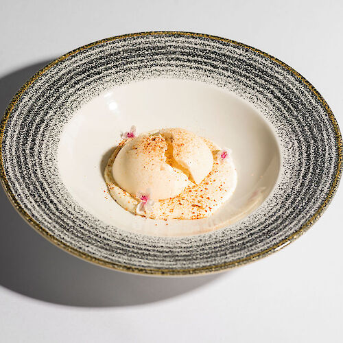 A plated dessert featuring a scoop of ice cream with pink and orange garnish, in a textured bowl.