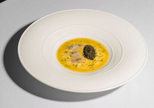 A gourmet dish featuring a yellow sauce, possibly a custard, with herbs and a small heap of black caviar on top, elegantly plated.