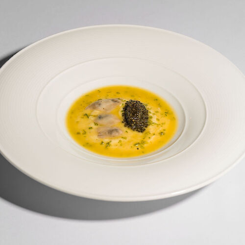 A gourmet dish featuring a yellow sauce, possibly a custard, with herbs and a small heap of black caviar on top, elegantly plated.