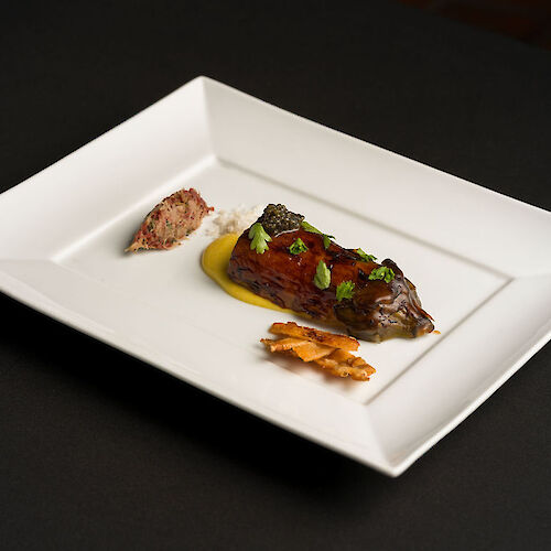 A rectangular plate with a gourmet dish: meat with garnish, sauce, and a small side serving, elegantly presented.