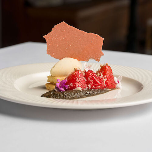 A plated dessert with watermelon, ice cream, a cracker, cream, and decorative elements, served on a white plate.