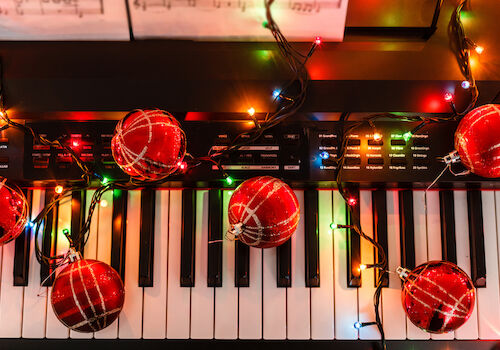 A keyboard decorated with colorful Christmas lights and red ornaments, creating a festive atmosphere and a musical holiday vibe.