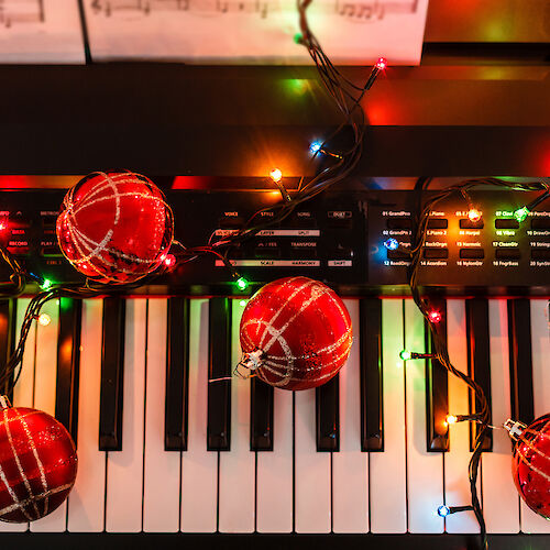 A keyboard decorated with colorful Christmas lights and red ornaments, creating a festive atmosphere and a musical holiday vibe.