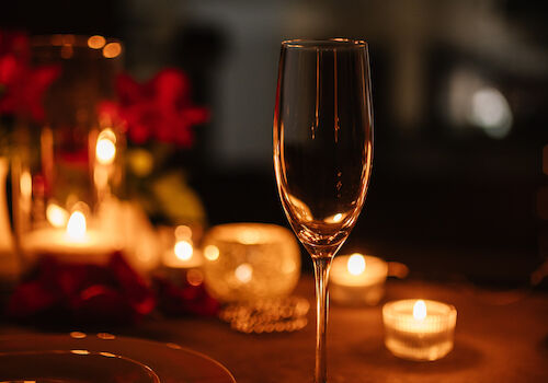 A dimly lit table with a champagne glass, plates, and candles, surrounded by small floral decorations, creating a romantic ambiance.