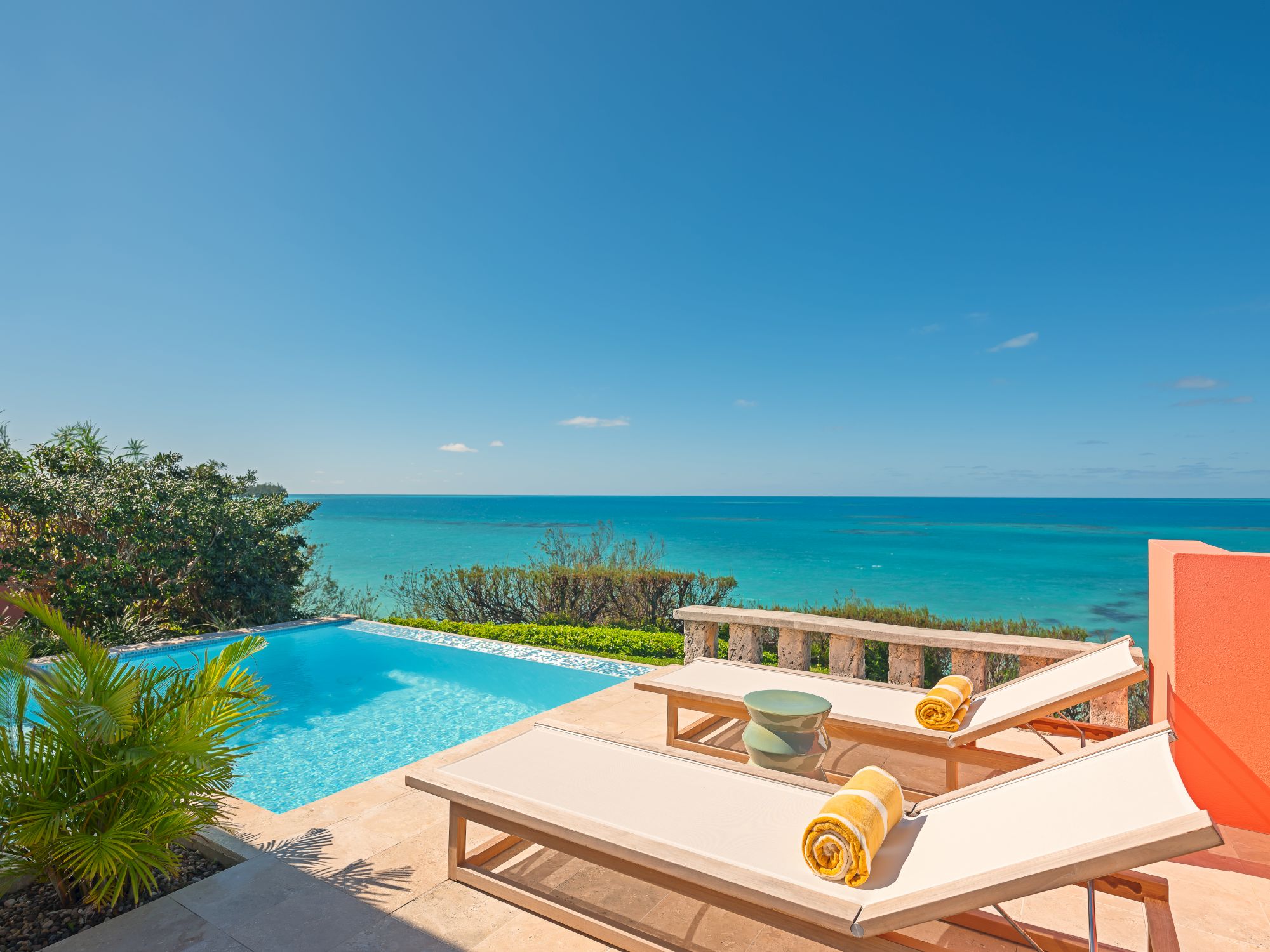 Ocean view from a poolside patio with loungers and towels.