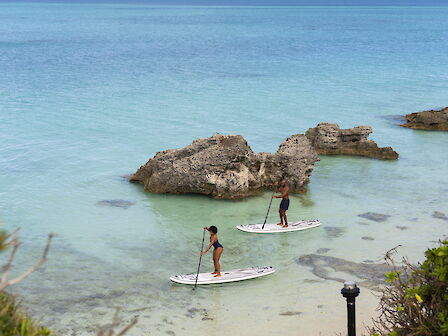 Two people on paddleboards navigate clear waters near rocky formations, surrounded by lush greenery.