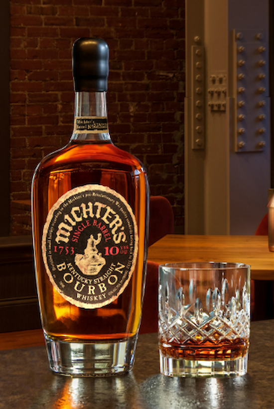 A bottle of Michter's 10 Year Bourbon with a glass sits on a bar counter in a cozy, dimly lit setting with city views outside.