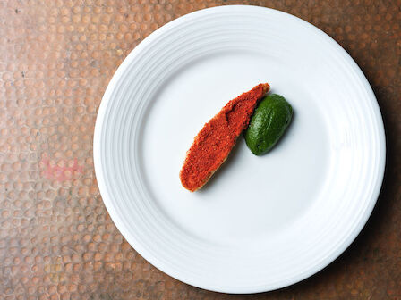 A white plate with a red sauce-covered item and a green vegetable arranged neatly on it.